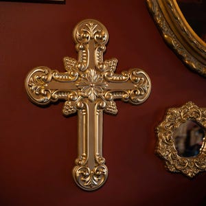 Könnte beinhalten: Ein verziertes goldenes Kreuz mit filigranen Details vor einem roten Hintergrund.