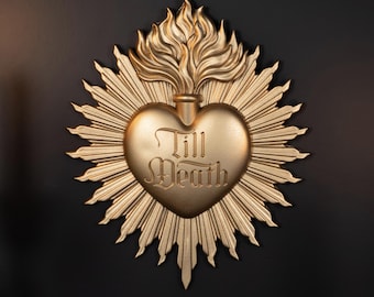 May include: A gold-colored wall plaque shaped like a sacred heart with a flame at the top and radiating sunburst rays. The center of the heart features the embossed text Till Death in a gothic-style font, creating a textured metallic appearance.