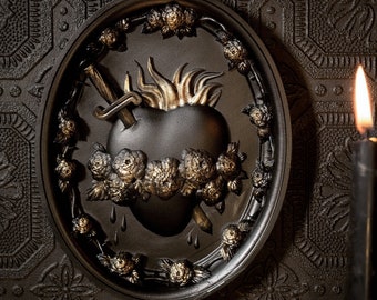 Può includere: Una targa da parete decorativa nera e dorata con un cuore stilizzato trafitto da un pugnale, circondato da spine e rose.