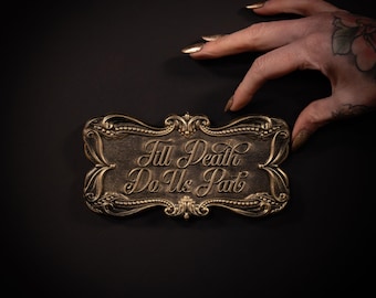 May include: A rectangular plaque with ornate, raised gold-toned borders and a dark, textured center. The text 'Till Death Do Us Part' is embossed in a flowing, elegant script font across the middle of the plaque, creating a high-contrast look.