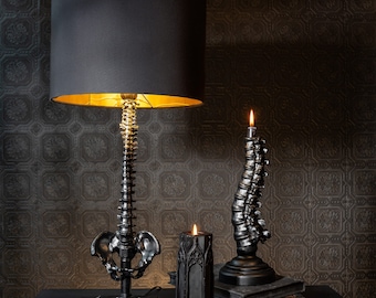 May include: Two black table lamps with a skeletal spine design. One lamp has a black lampshade and the other has a black candle.
