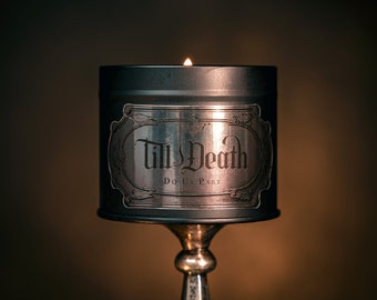 May include: A silver candle tin with a black label that reads "Till Death Do Us Part". The candle is lit and the flame is visible.