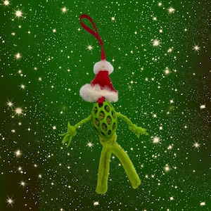 May include: A green plush toy shaped like a turtle wearing a red and white Santa hat. The toy is against a green background with white stars.