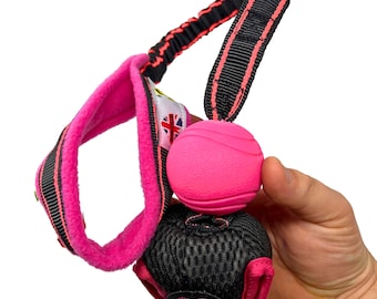 Pode incluir: Brinquedo para cachorro rosa com uma bolsa de malha preta e uma bola rosa presa a uma alça preta e rosa. A bola tem uma superfície texturizada.