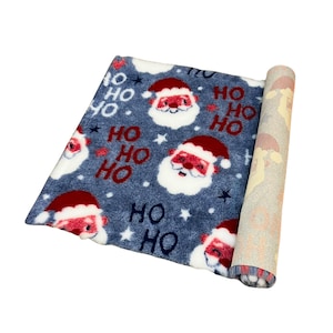 May include: A rolled-up Christmas rug with a blue background. The rug features Santa Claus faces, white stars, and the words "HO HO" in red. The rolled-up section reveals a beige underside with a red and white pattern.