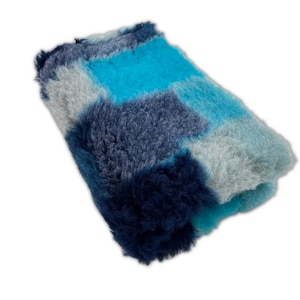 May include: A soft, plush blanket with a patchwork design in shades of blue, grey, and white.