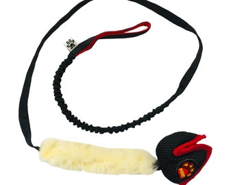Pode incluir: Um brinquedo para cães preto e vermelho com uma faixa de lã branca e uma trela de bungee. O brinquedo tem uma bola de malha com as palavras "Paws Power" impressas nela.