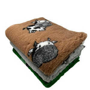 May include: A stack of three plush blankets with a cow print design. The top blanket is brown, the middle blanket is grey, and the bottom blanket is green.