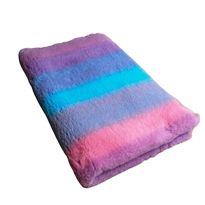 May include: A folded, rectangular plush blanket with horizontal stripes of colour. The stripes transition from pink to purple, with a band of turquoise blue in the centre. The blanket has a soft, fuzzy texture.