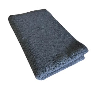 Puede incluir: Una alfombra de baño gris oscuro hecha de material suave y esponjoso. La alfombra está doblada por la mitad y tiene una superficie texturizada.