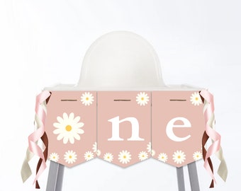 Op de afbeelding: Roze en witte hoge stoel banner met het woord "one" in witte letters en een madeliefjespatroon. De banner heeft bruine lintjes.