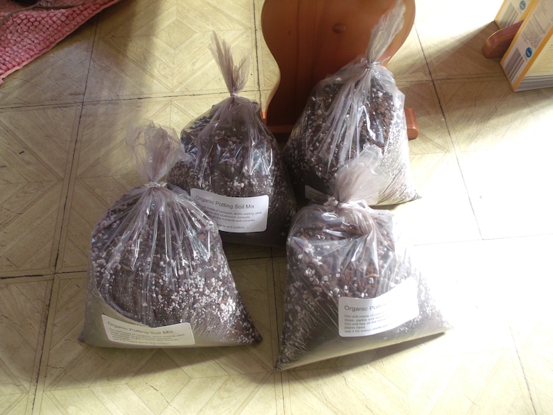 Pu&ograve; includere: Quattro sacchetti di plastica trasparenti riempiti di terriccio marrone. I sacchetti sono etichettati "Organic Potting Soil Mix".