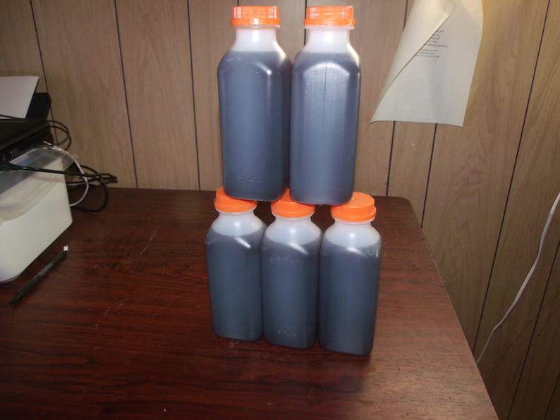Pu&ograve; includere: Sei bottiglie di plastica trasparente piene di un liquido scuro, impilate a forma di piramide. Le bottiglie hanno corpi bianchi e tappi arancioni. Le bottiglie sono su una superficie di legno marrone scuro.