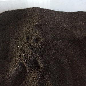 Pu&ograve; includere: Primo piano di materiale marrone scuro, finemente macinato, possibilmente terra o compost, che riempie un contenitore di plastica trasparente. La consistenza appare granulare e leggermente irregolare, con sottili variazioni di tono. L'impressione generale &egrave; di una sostanza naturale e organica.