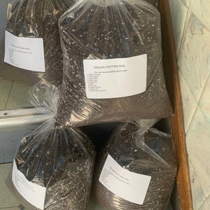 May include: Four clear plastic bags filled with dark brown potting soil. Each bag has a white label that reads "Organic Potting Soil" and lists the ingredients.