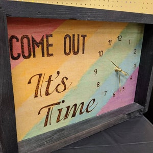 May include: A wooden clock with a rainbow-colored background and the text "COME OUT It's Time". The clock hands are set to 3:45.
