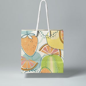 May include: A white paper shopping bag with a colorful fruit pattern. The pattern features lemons, limes, strawberries, and a green melon. The bag has white rope handles.