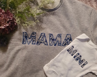 May include: A gray sweatshirt with the word "MAMA" in blue and white patterned letters. A white onesie with the word "MINI" in blue and white patterned letters.