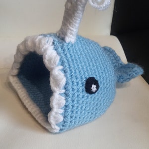 May include: A blue crocheted whale with a white crocheted spout and a black eye. The whale is a small, handmade toy.