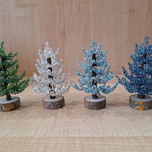 K&ouml;nnte beinhalten: Vier Perlen-Weihnachtsb&auml;ume in verschiedenen Farben: gr&uuml;n, wei&szlig;, hellblau und dunkelblau. Die B&auml;ume sind alle gleich gro&szlig; und haben einen Holzsockel.