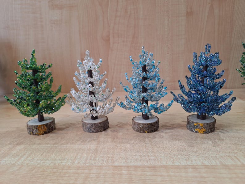 K&ouml;nnte beinhalten: Vier Perlen-Weihnachtsb&auml;ume in verschiedenen Farben: gr&uuml;n, wei&szlig;, hellblau und dunkelblau. Die B&auml;ume sind alle gleich gro&szlig; und haben einen Holzsockel.