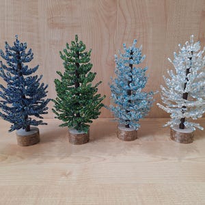 K&ouml;nnte beinhalten: Vier Perlen-Weihnachtsb&auml;ume in verschiedenen Farben: Blau, Gr&uuml;n, Hellblau und Wei&szlig;. Die B&auml;ume sind alle gleich gro&szlig; und stehen auf einer Holzoberfl&auml;che.
