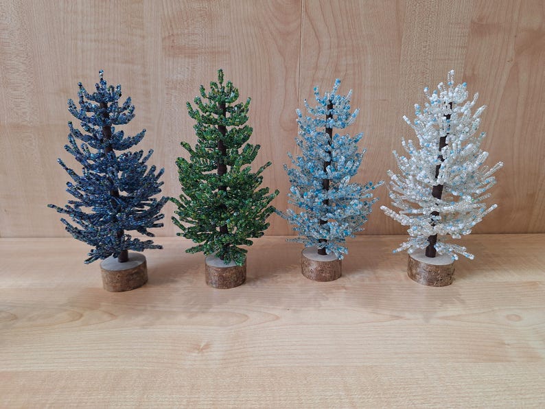 K&ouml;nnte beinhalten: Vier Perlen-Weihnachtsb&auml;ume in verschiedenen Farben: Blau, Gr&uuml;n, Hellblau und Wei&szlig;. Die B&auml;ume sind alle gleich gro&szlig; und stehen auf einer Holzoberfl&auml;che.
