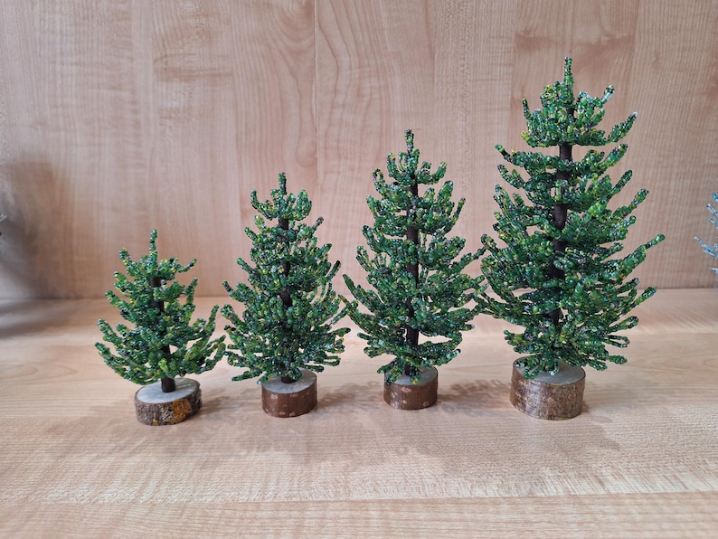 K&ouml;nnte beinhalten: Vier gr&uuml;ne Perlen-Weihnachtsb&auml;ume in verschiedenen Gr&ouml;&szlig;en, jeder mit einer braunen Holzbasis.