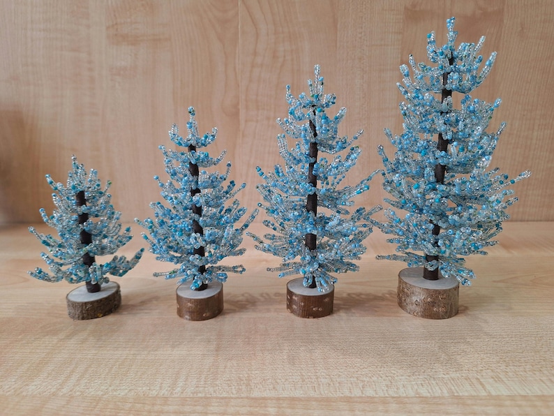 K&ouml;nnte beinhalten: Vier blaue und wei&szlig;e Perlen-Weihnachtsb&auml;ume in verschiedenen Gr&ouml;&szlig;en auf einer Holzoberfl&auml;che.