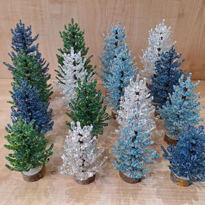 K&ouml;nnte beinhalten: Eine Sammlung von neun Weihnachtsb&auml;umen aus Perlen in verschiedenen Blaut&ouml;nen, Gr&uuml;n- und Wei&szlig;t&ouml;nen. Die B&auml;ume sind alle etwa 25 cm hoch und aus kleinen Perlen gefertigt.