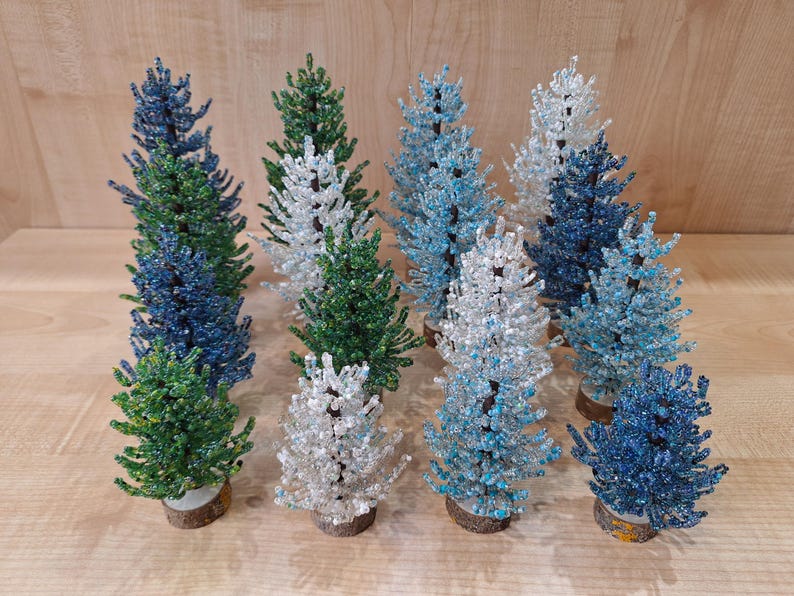 K&ouml;nnte beinhalten: Eine Sammlung von neun Weihnachtsb&auml;umen aus Perlen in verschiedenen Blaut&ouml;nen, Gr&uuml;n- und Wei&szlig;t&ouml;nen. Die B&auml;ume sind alle etwa 25 cm hoch und aus kleinen Perlen gefertigt.