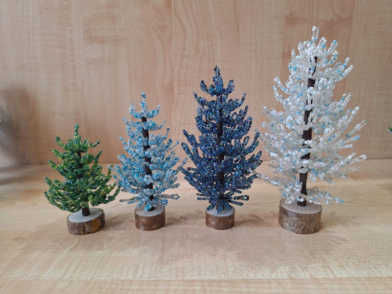 K&ouml;nnte beinhalten: Vier Perlen-Weihnachtsb&auml;ume, ein gr&uuml;ner, zwei blaue und ein wei&szlig;er, auf einer Holzoberfl&auml;che.
