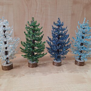 K&ouml;nnte beinhalten: Vier Perlen-Weihnachtsb&auml;ume in verschiedenen Farben: Wei&szlig;, Gr&uuml;n, Blau und Hellblau. Die B&auml;ume stehen alle auf Holzsockeln.