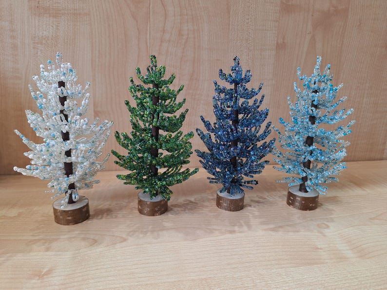 K&ouml;nnte beinhalten: Vier Perlen-Weihnachtsb&auml;ume in verschiedenen Farben: Wei&szlig;, Gr&uuml;n, Blau und Hellblau. Die B&auml;ume stehen alle auf Holzsockeln.