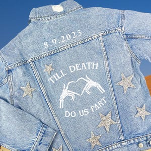 May include: A light blue denim jacket with the text "Till Death Do Us Part" and a skeleton hand heart design. The jacket has silver glitter stars on the back.