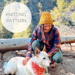 May include: A woman wearing a yellow knit beanie and a plaid shirt is kneeling next to a white and brown dog wearing a red bandana. The text "KNITTING PATTERN" is written in a white circle in the upper left corner of the image.