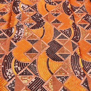May include: Orange, brown, and gold sequined fabric with a geometric pattern of circles, squares, and triangles.