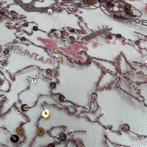 May include: Pink and gold sequined fabric with a delicate floral pattern. The fabric is sheer and has a soft, flowing texture.