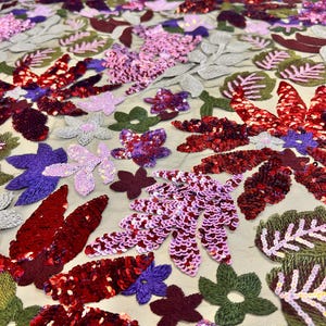 May include: Close-up of a fabric with a floral design. The fabric features embroidered leaves and flowers in shades of red, pink, purple, and green. The background is a light beige color, and the fabric appears to be sheer.