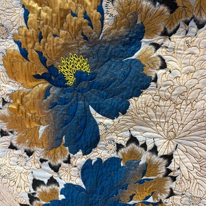 May include: A white fabric with a blue and gold floral pattern. The flowers are large and have a textured appearance. The fabric is likely a kimono or other traditional Japanese garment.
