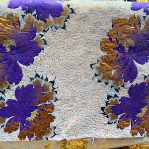 May include: White fabric with a repeating pattern of purple and gold flowers. The flowers have a textured, almost metallic look.
