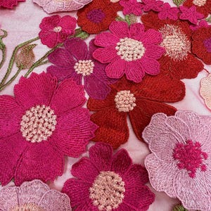 May include: Pink, red, and fuchsia embroidered flowers on a sheer pink mesh fabric. The flowers are layered and have a 3D effect.