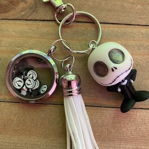 May include: A silver charm bracelet with a white tassel charm, a silver charm with a clear glass circle containing black and white Jack Skellington faces, and a silver charm with a Jack Skellington character.