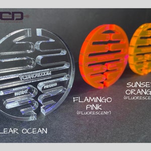 May include: Clear acrylic and fluorescent pink and orange laser-cut designs. The clear design has the text "VCDNOW.COM" and "PATENT". The pink and orange designs are labeled "FLAMINGO PINK" and "SUNSET ORANGE" respectively.
