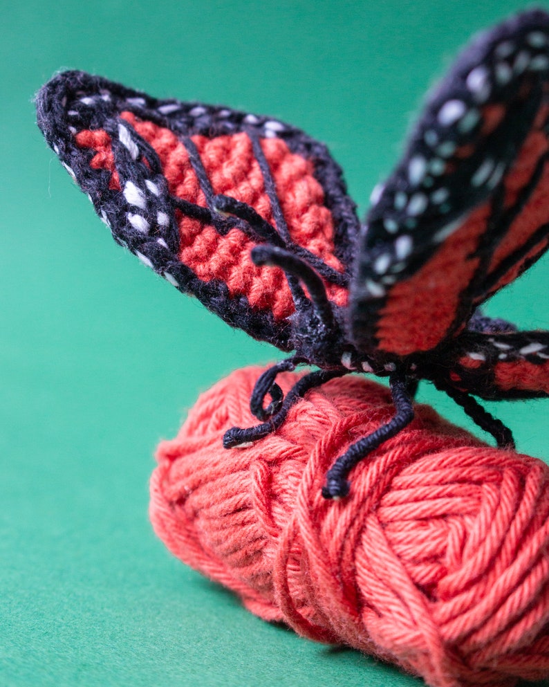 May include: A crocheted butterfly with black and red wings perched on a ball of red yarn.