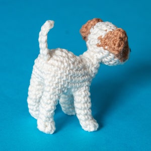May include: A white crocheted dog toy with brown ears. The dog is standing on a blue background.