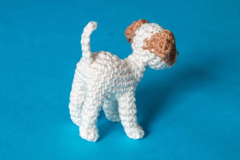 May include: A white crocheted dog toy with brown ears. The dog is standing on a blue background.