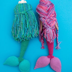 May include: Two crocheted mermaid dolls with long, colorful hair. One doll has a green tail and the other has a pink tail.