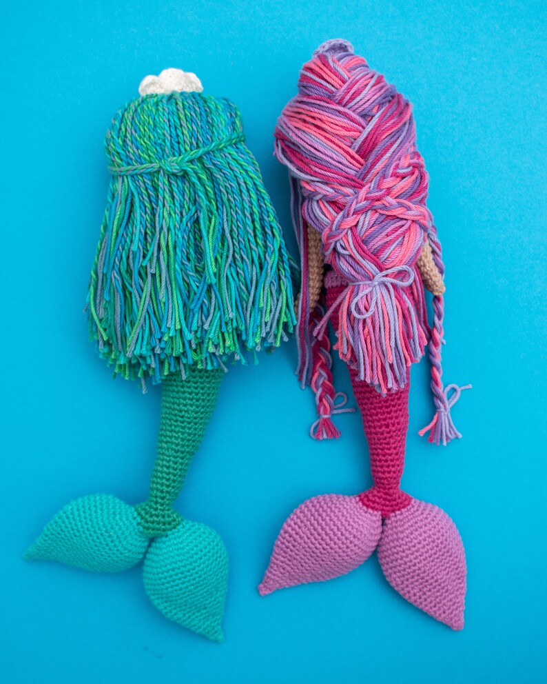 May include: Two crocheted mermaid dolls with long, colorful hair. One doll has a green tail and the other has a pink tail.