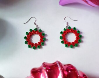 May include: A pair of red and green paper quilled earrings shaped like a wreath. The earrings are hanging from silver hooks.